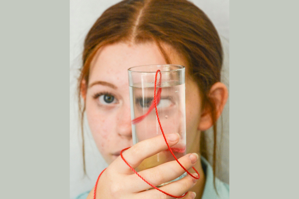 A girl holding a glass of drinking water in front of her face.