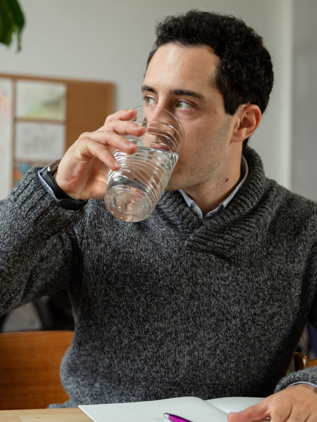 A man sitting on a chair and drinking water through a big glass.