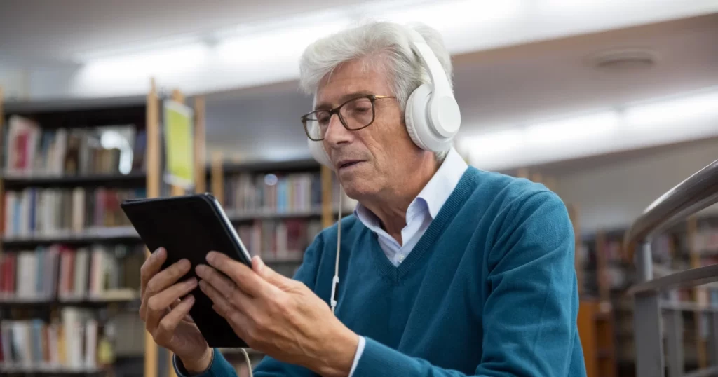 US senior leanring a new language online on a tab with headphones on. 