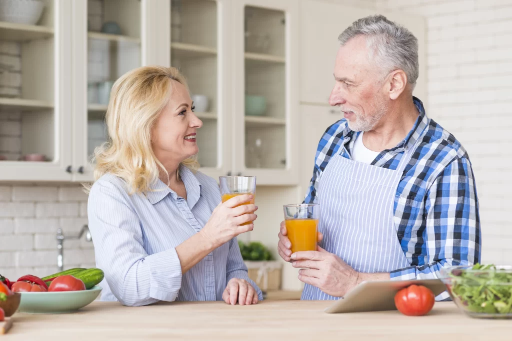 Senior couple holding glass juice in the kitchen.